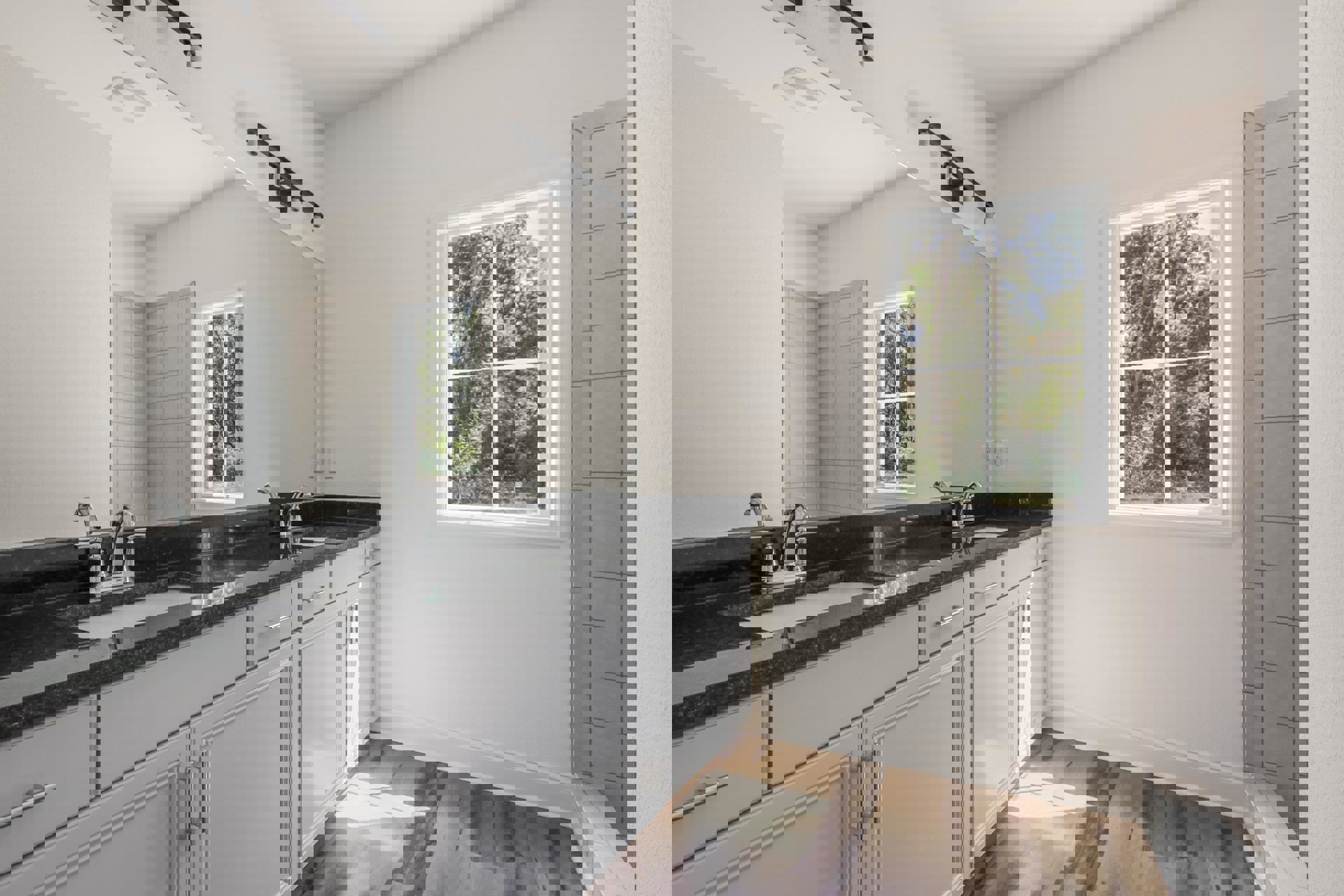 Modern bathroom featuring a white cabinet and countertop, rectangular mirror above the sink, black track lighting, white door with matching frame, and window overlooking leafy