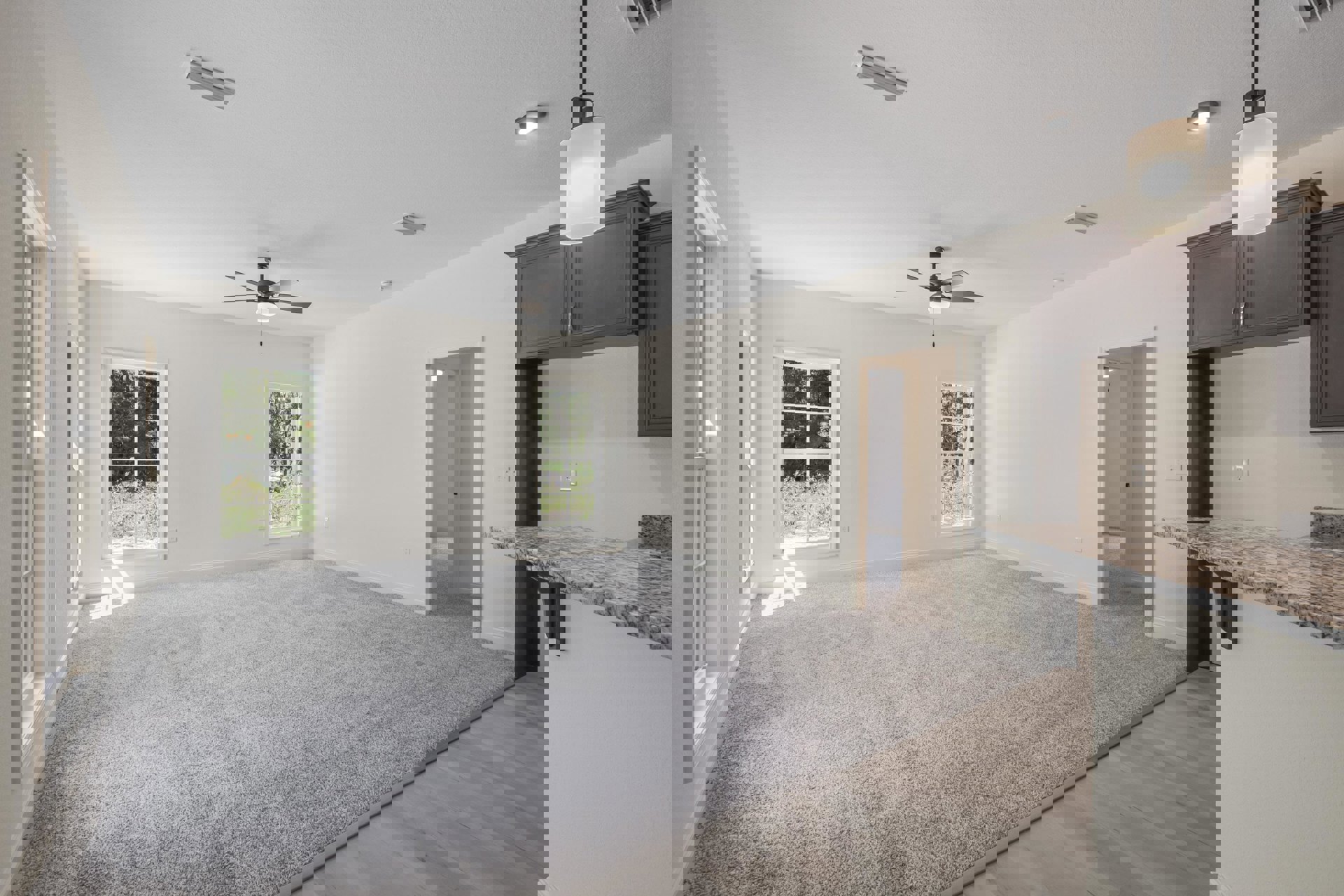 Living room with multi-pane window overlooking forest, stone fireplace, ceiling fan, carpet flooring, wall sconce, granite countertop, and tile accents