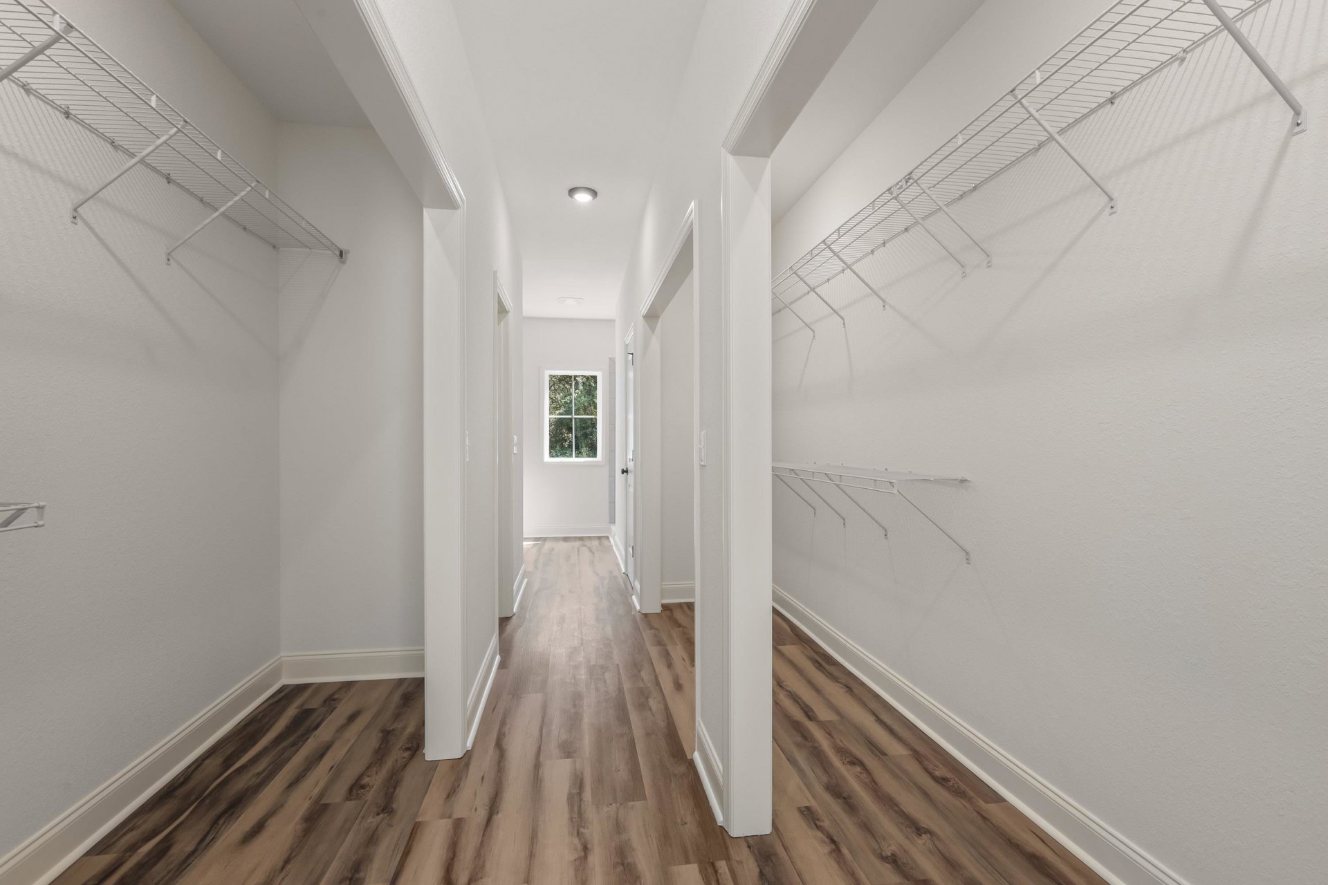 Hallway with white plaster walls, built-in white shelves, wood flooring, and a window with a white frame