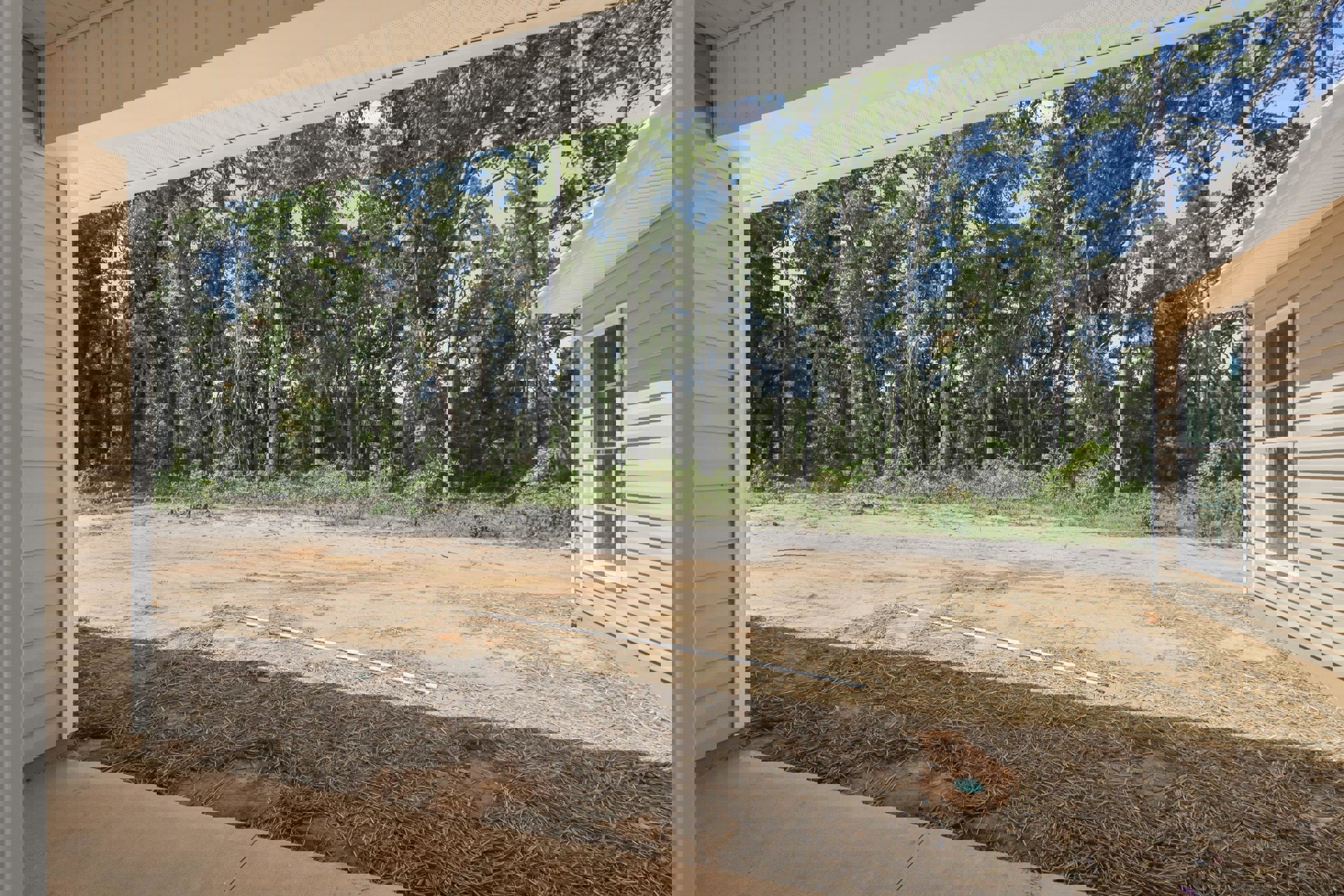 White roof and overhang above porch, window with trim, dirt area covered in straw, trees and sky in background