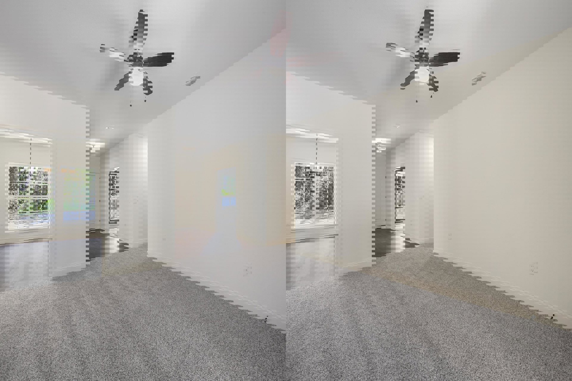 Carpeted bedroom with white walls, ceiling fan with light, window showing trees and grass, white door with black handle