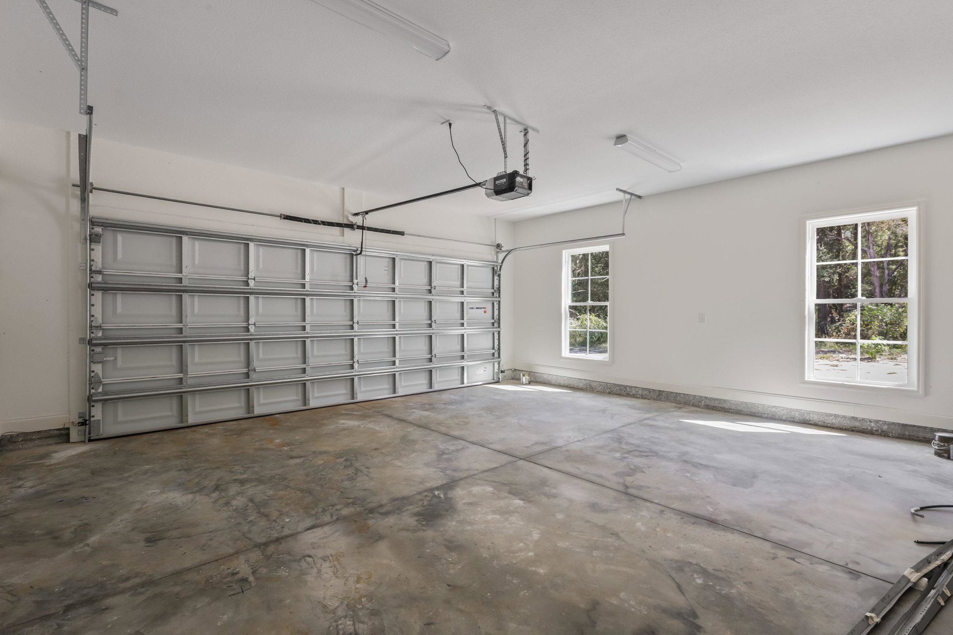 Garage interior with plaster walls, large window overlooking trees, concrete floor, and sectional garage door with visible pipe fixture