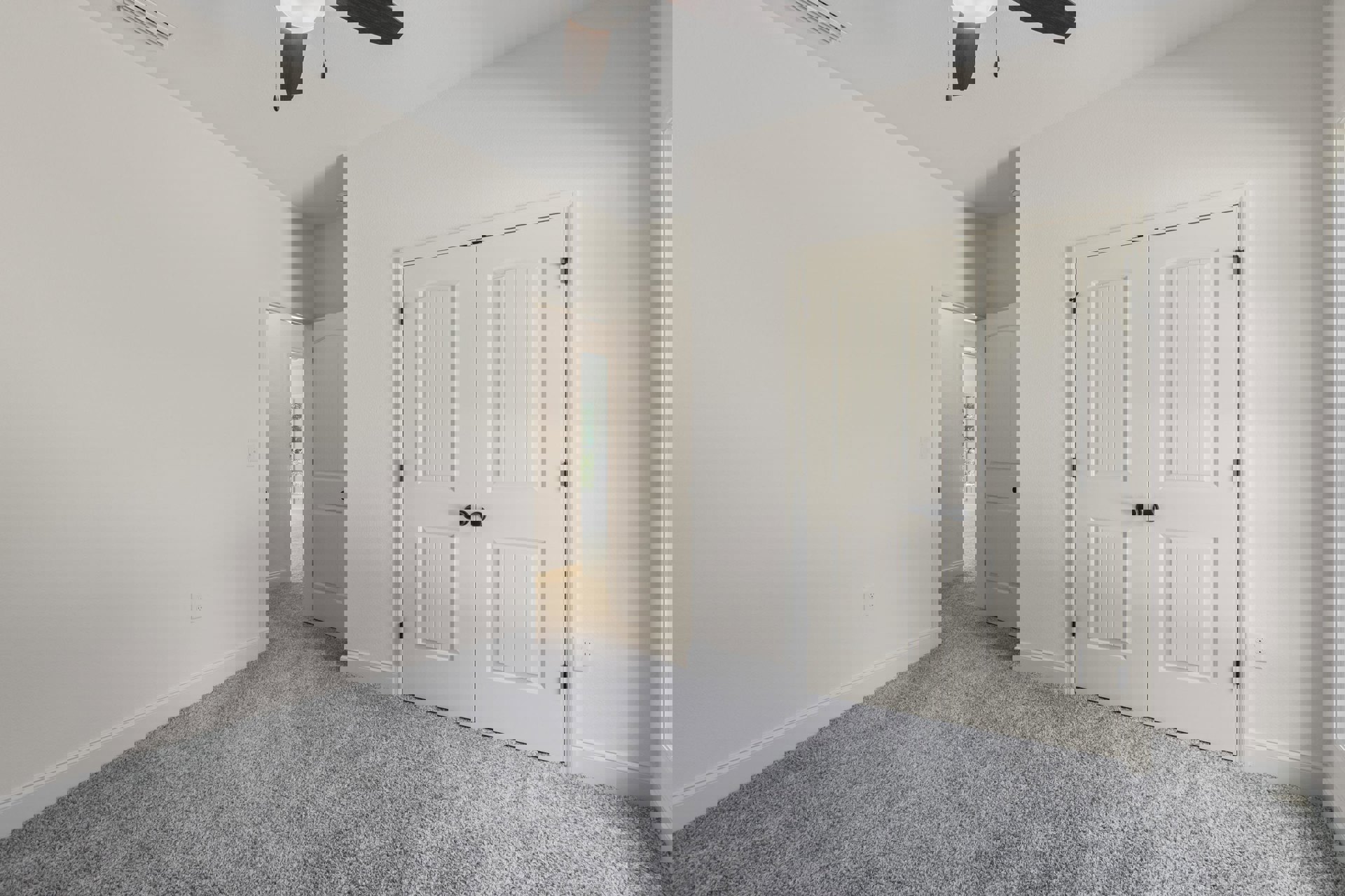 Bedroom with plush beige carpet, white paneled doors featuring black handles, white walls, and a ceiling fan with a central light fixture