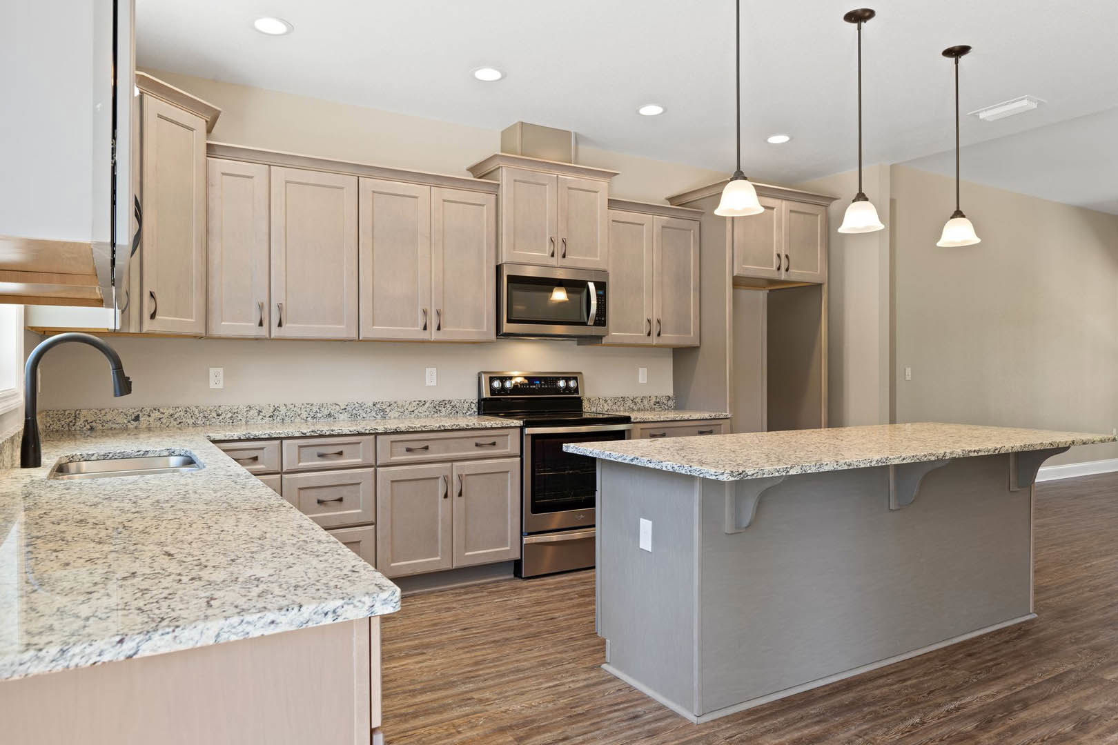 Granite countertops, stainless steel oven and microwave, white cabinetry, black faucet, pendant lighting above kitchen island