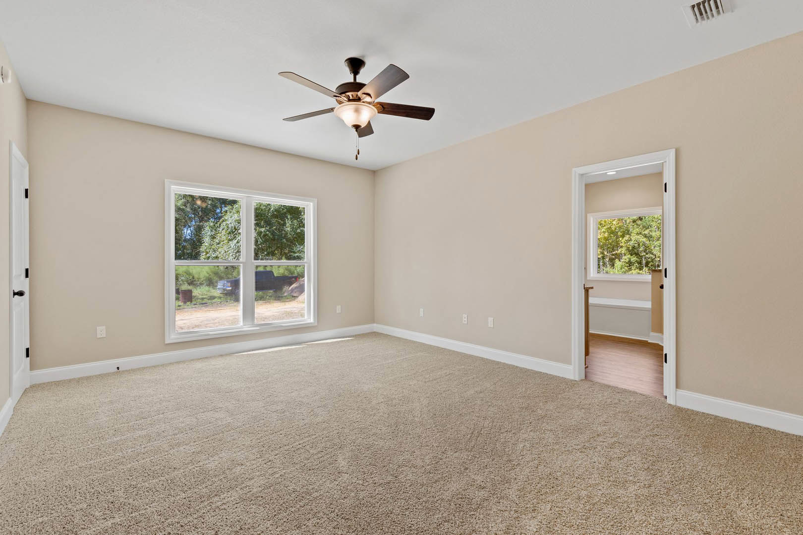 Carpeted room with white walls, ceiling fan with light fixture, large window showing trees and a parked truck outside