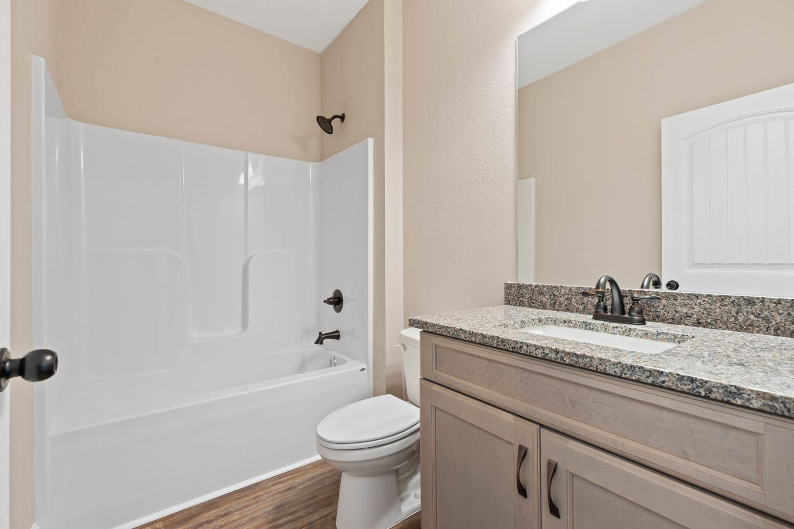 Bathroom with white tile walls, white bathtub, closed white toilet, modern black shower head, white sink with chrome faucet, and white door visible in foreground