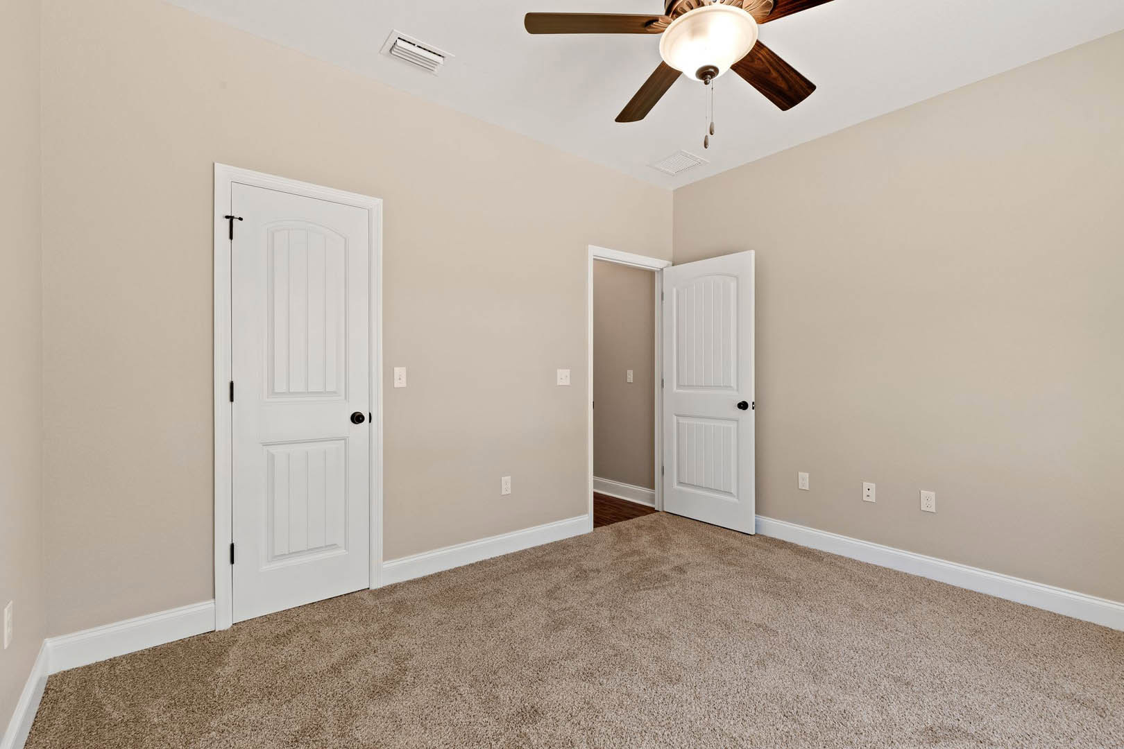 Carpeted room with white paneled doors, black hardware, ceiling fan with light, and light switch on neutral wall