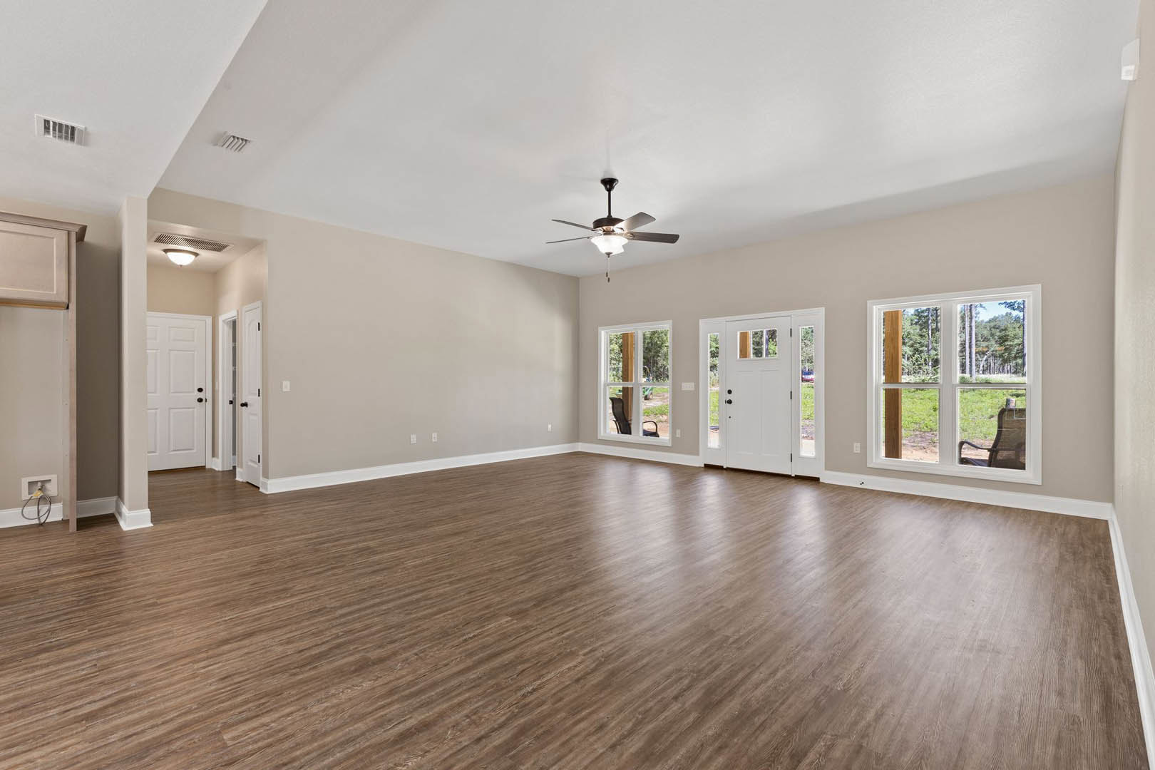 Spacious room with wood flooring, white walls, ceiling fan with light, multiple windows, and a white door with black knobs