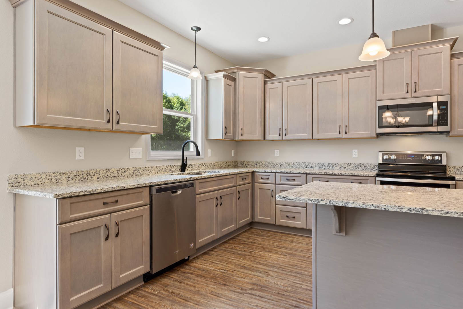 Granite countertops, wood cabinets, stainless steel microwave and oven, silver refrigerator, white light switch on wall, ceiling light fixture