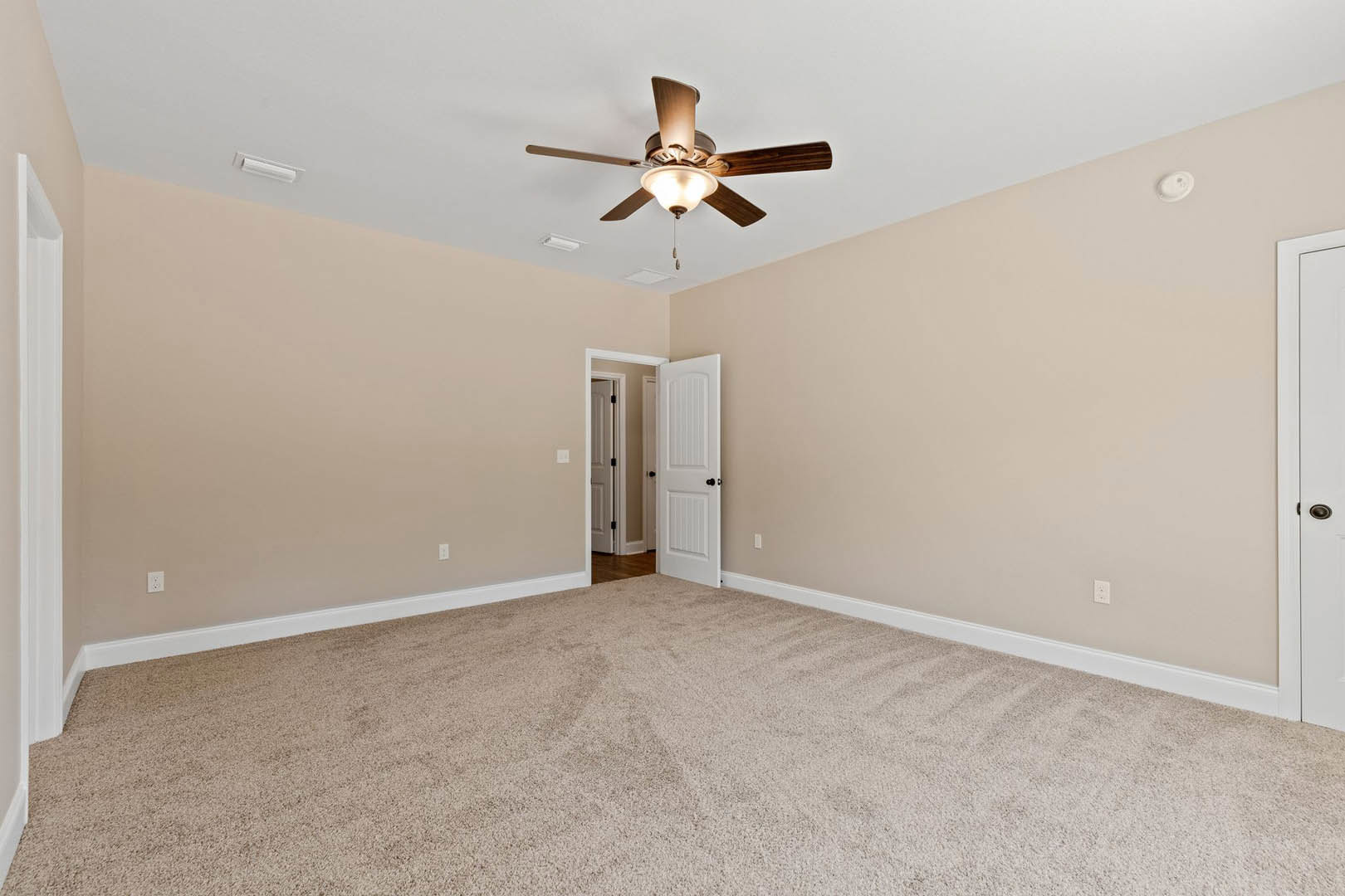 Bedroom with beige carpet flooring, white walls, ceiling fan with light fixture, white door featuring black hardware