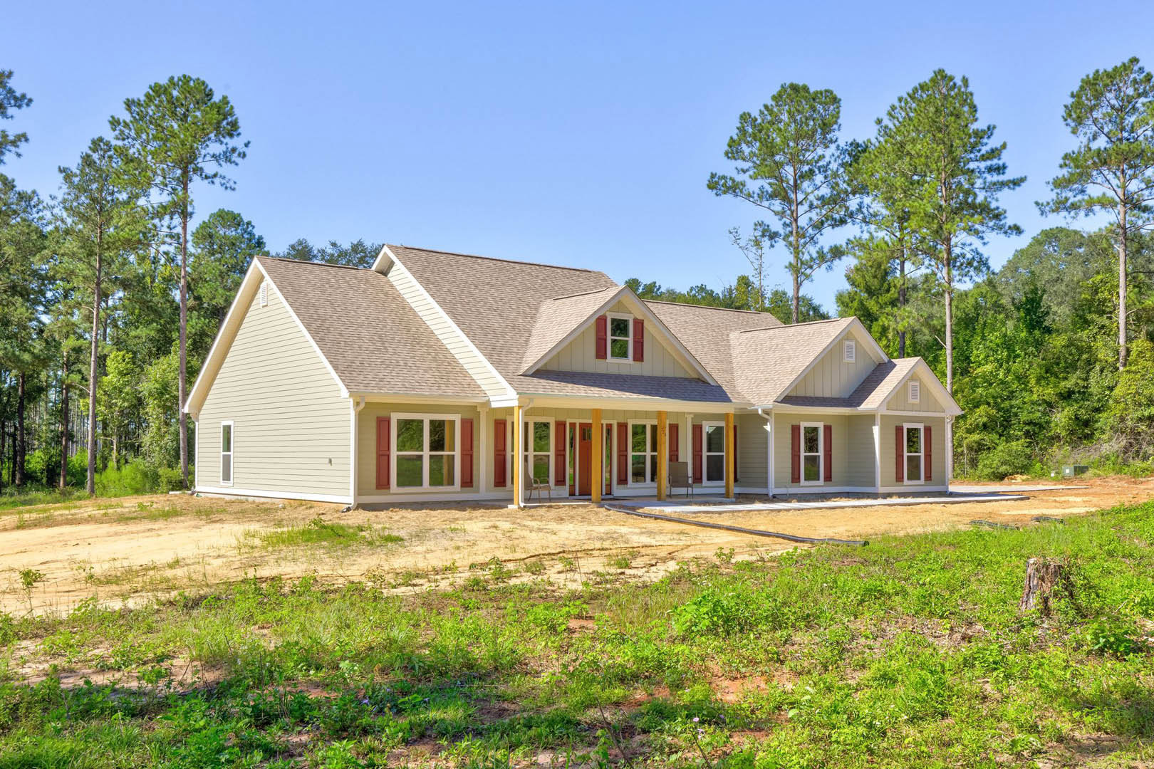 Two-story house with white-framed windows, covered front porch featuring a chair, expansive grassy front yard, mature tree and tree stump near the property.