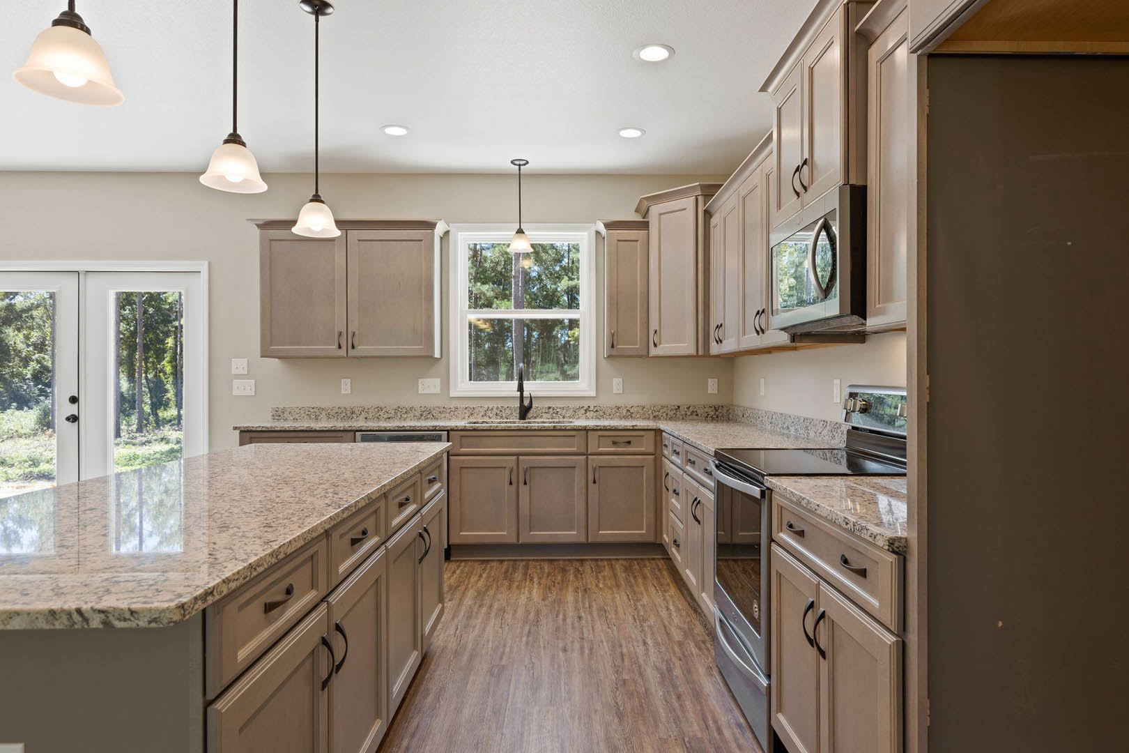Granite countertops and wood-grained flooring in a kitchen with white cabinetry, stainless steel appliances, a window above the sink, and pendant lighting fixtures