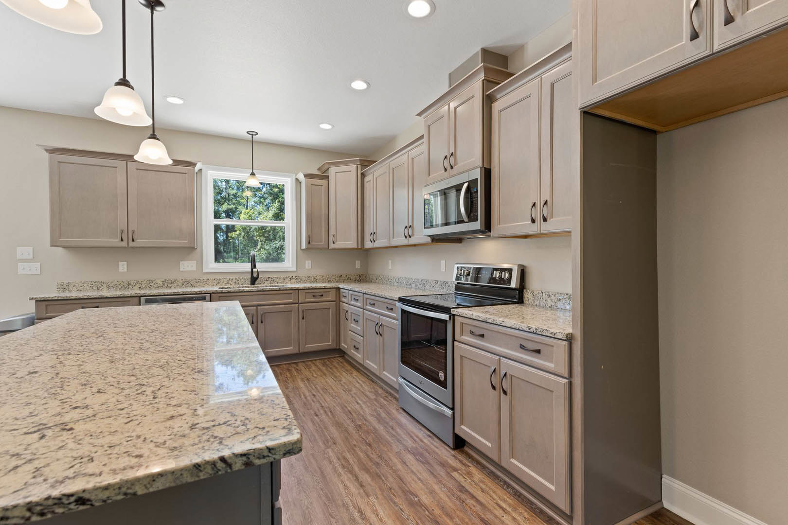 Granite countertops, stainless steel stove and oven, microwave with glass door, marble-topped island, white cabinetry, window with ceiling light fixture, light-colored flooring