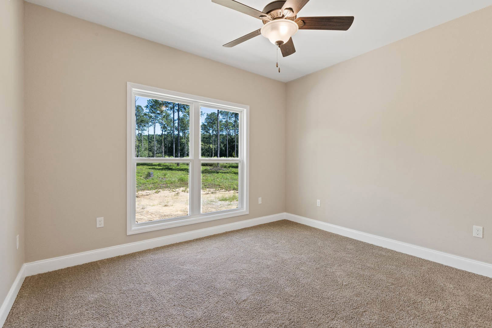 Carpeted room with white walls, ceiling fan with light fixture, large window showing green trees outside, crown molding along ceiling.