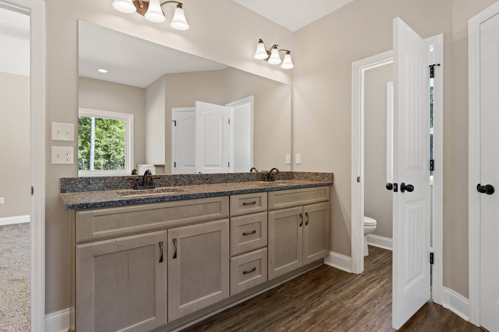 Bathroom featuring marble countertop, wood flooring, white cabinetry, undermount sink, and large window overlooking trees.