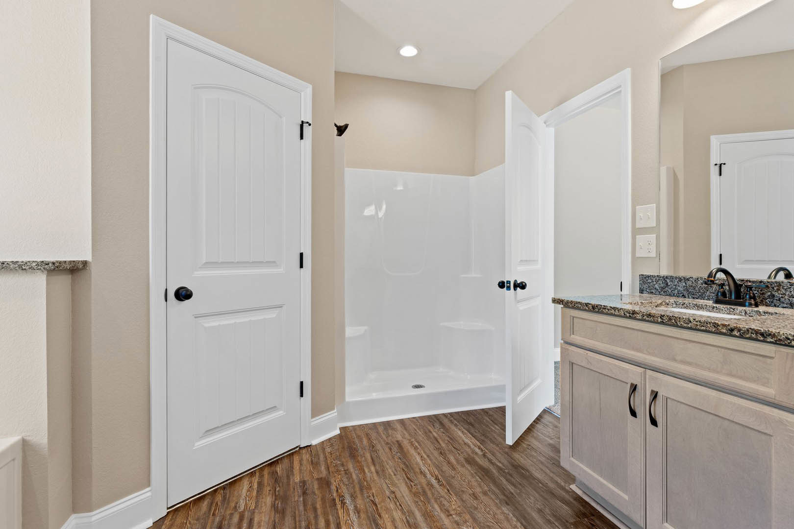 Bathroom with glass shower featuring black hardware, white vanity with undermount sink, wood flooring, white door with black knob, and white trim.