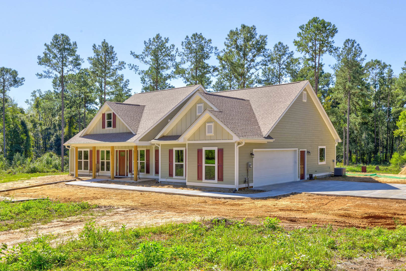 White two-story house with attached garage, paved driveway, green lawn, mature trees in the background, and large windows facing the yard