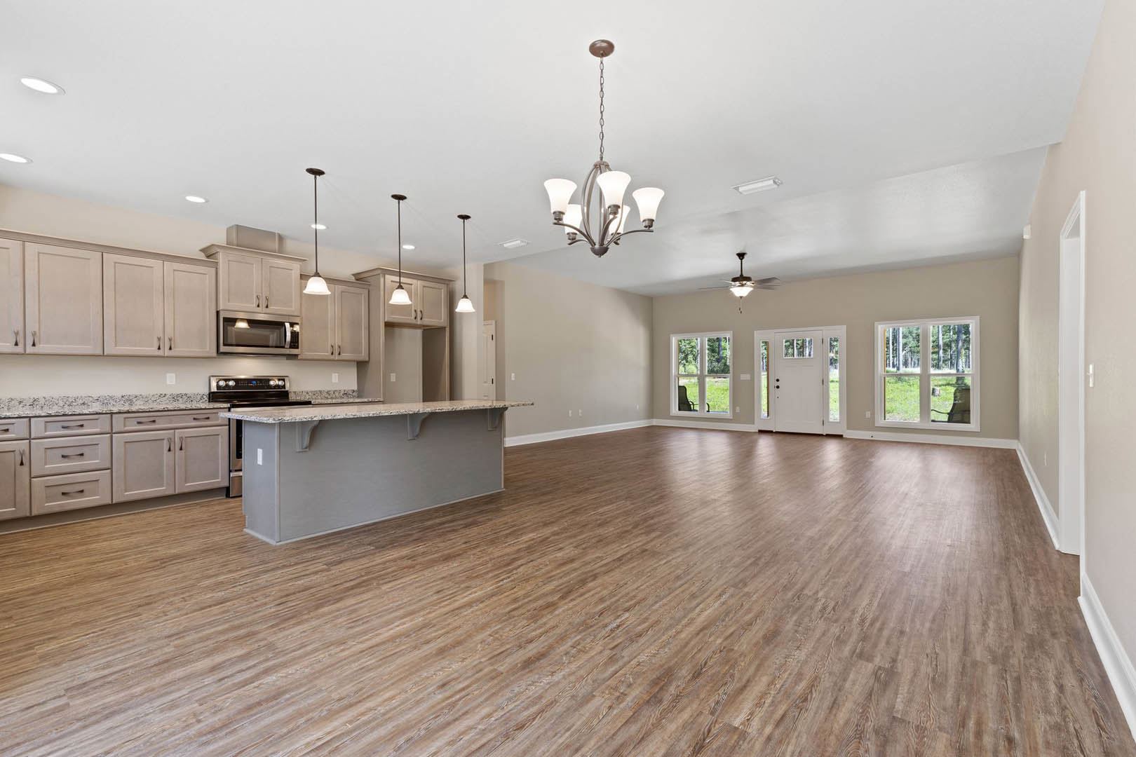 Spacious open-concept kitchen with central island, wood flooring, white cabinetry, stone countertops, stainless steel appliances, large windows, and modern chandelier hanging from