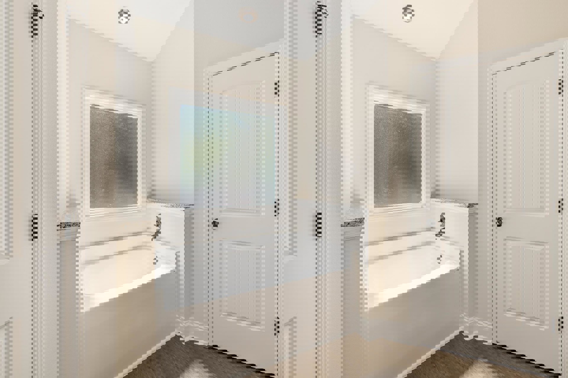 Freestanding white bathtub with chrome faucet, frosted window above, white paneled door with black knob, light fixture on ceiling, gray tile walls and floor