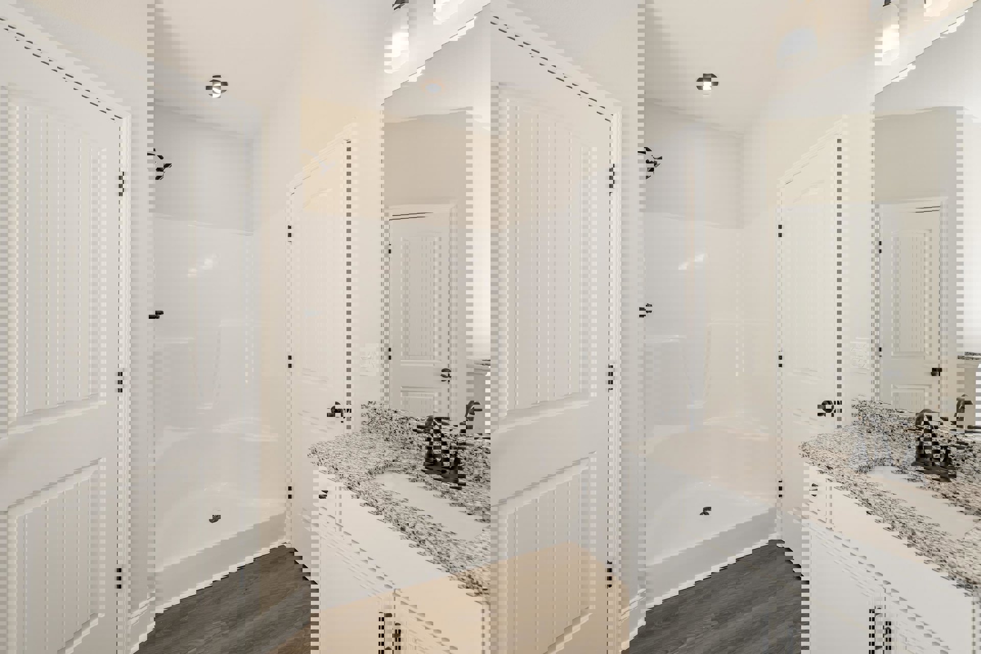 Bathroom with freestanding white bathtub, marble countertop vanity with black faucet, white cabinetry, white door with black handle, and tiled shower enclosure.