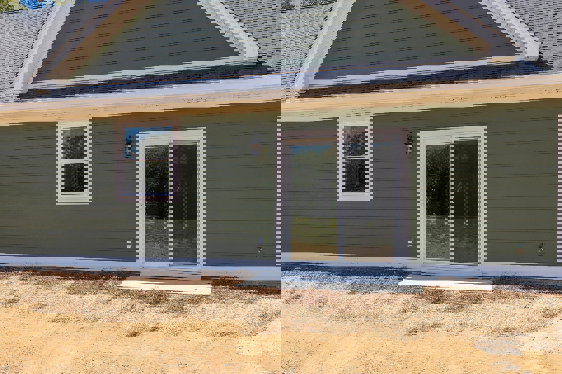 White-framed sliding glass door and window set in light-colored siding, cottage-style roof, landscaped ground in foreground