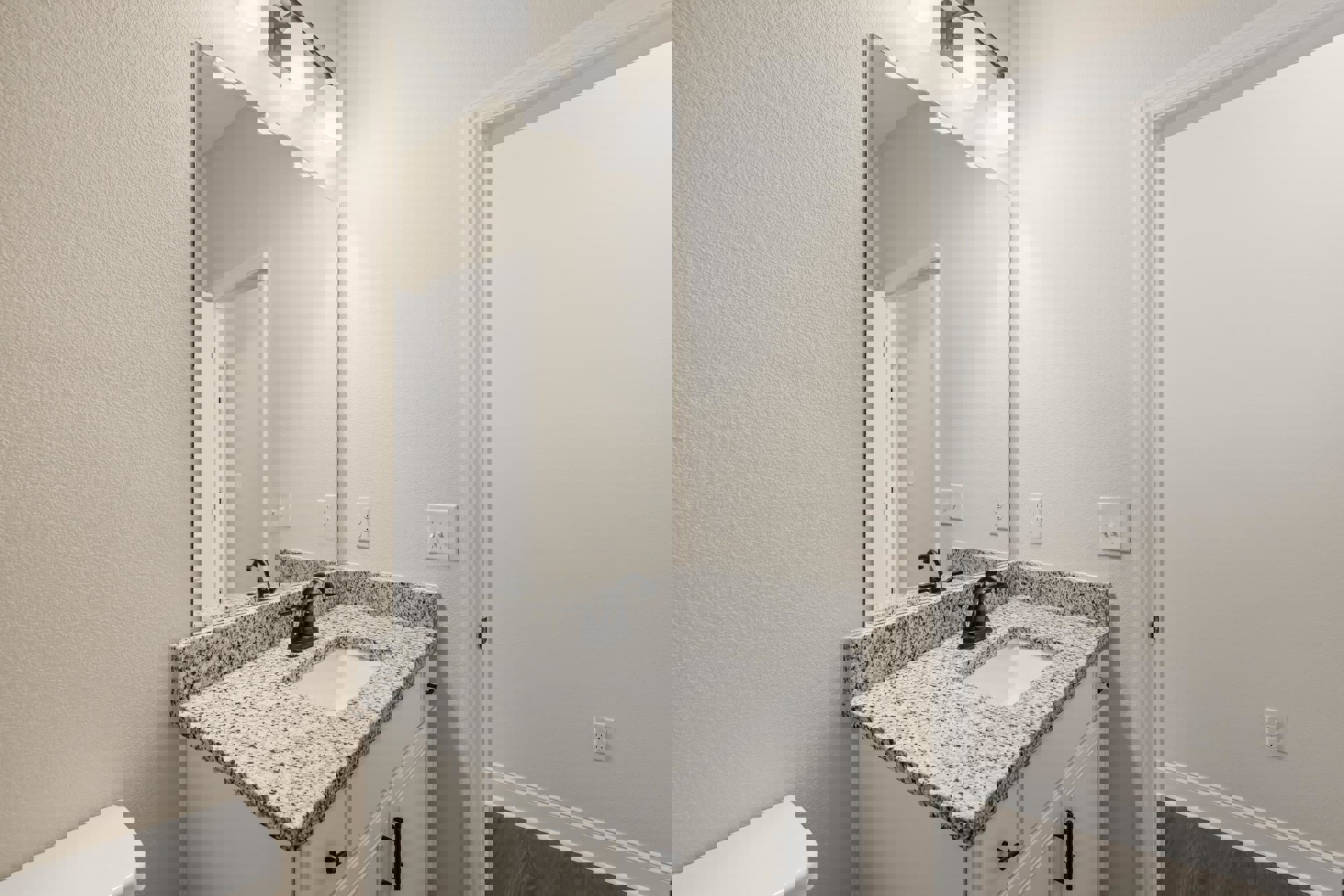 Marble countertop with undermount sink, large framed mirror above, white walls, chrome faucet, visible electrical outlet and double light switch.