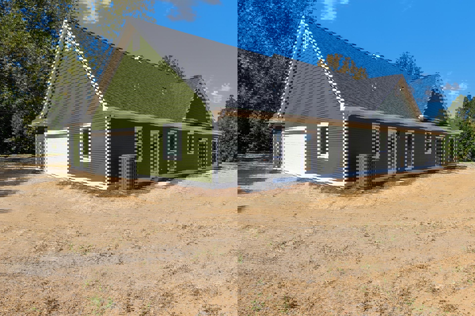 Green exterior wall with white garage door, large window reflecting lawn, grey utility box with red handle, tree and cloudy sky in background