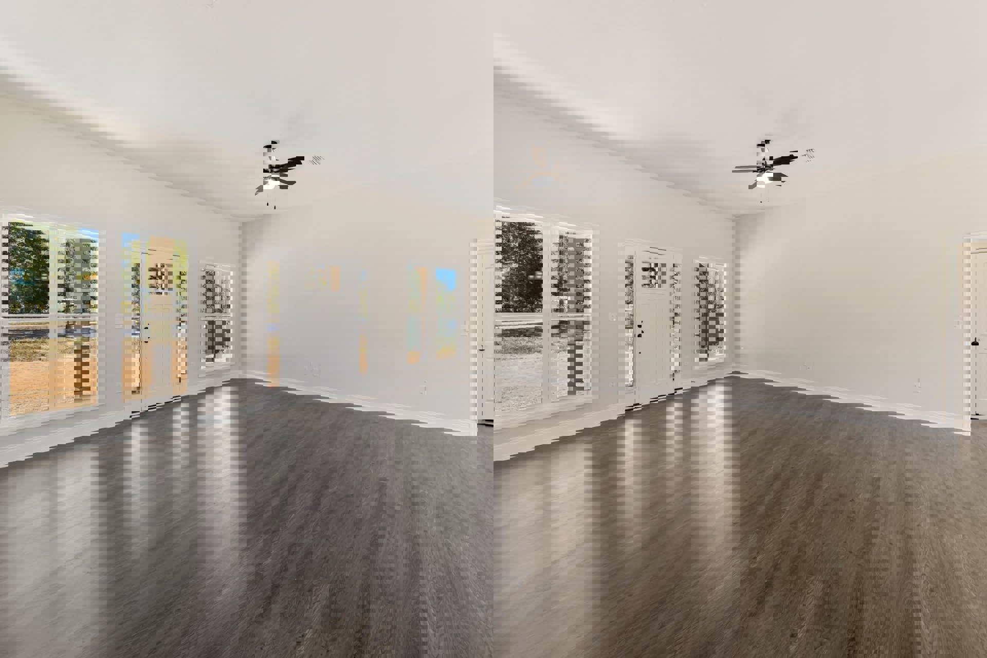 Spacious room with wood flooring, white plaster walls, ceiling fan with light fixture, large window overlooking trees, and white door with glass panels