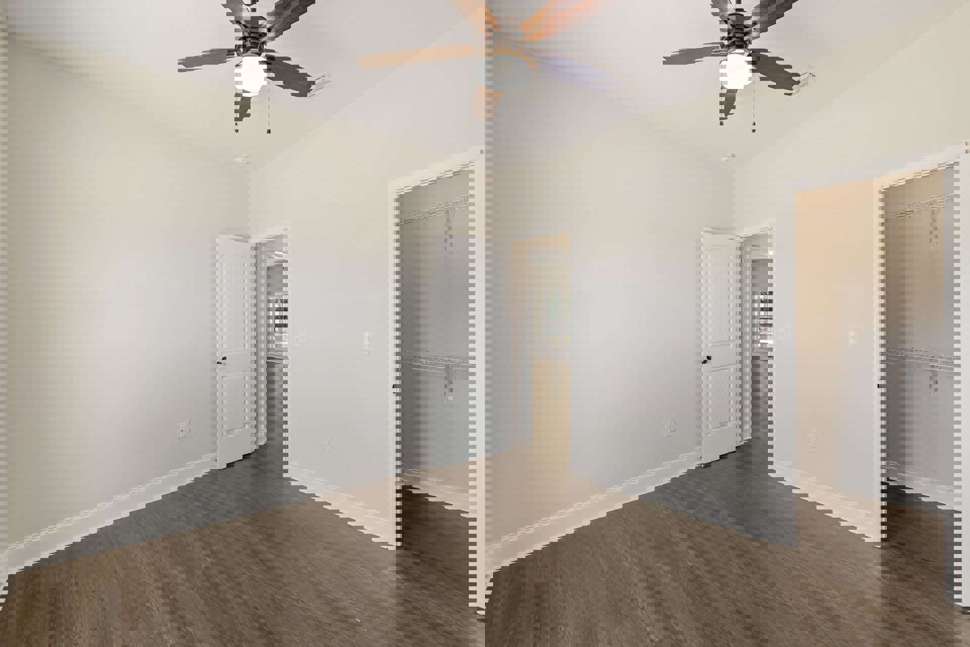 Ceiling fan with light fixture, wood laminate flooring, white walls, white door with black knob, open closet with overhead light, simple baseboard molding