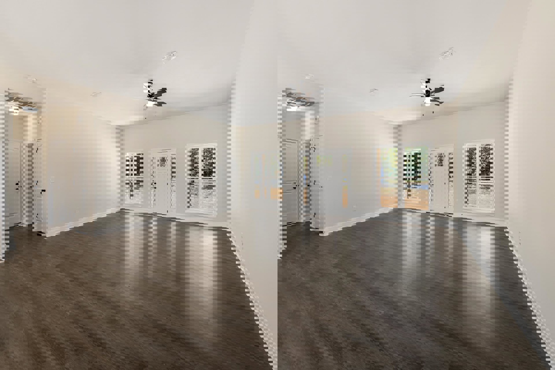 Spacious room with wood flooring, white plaster walls, ceiling fan with light, large window overlooking trees, and white door with glass panes and black knobs