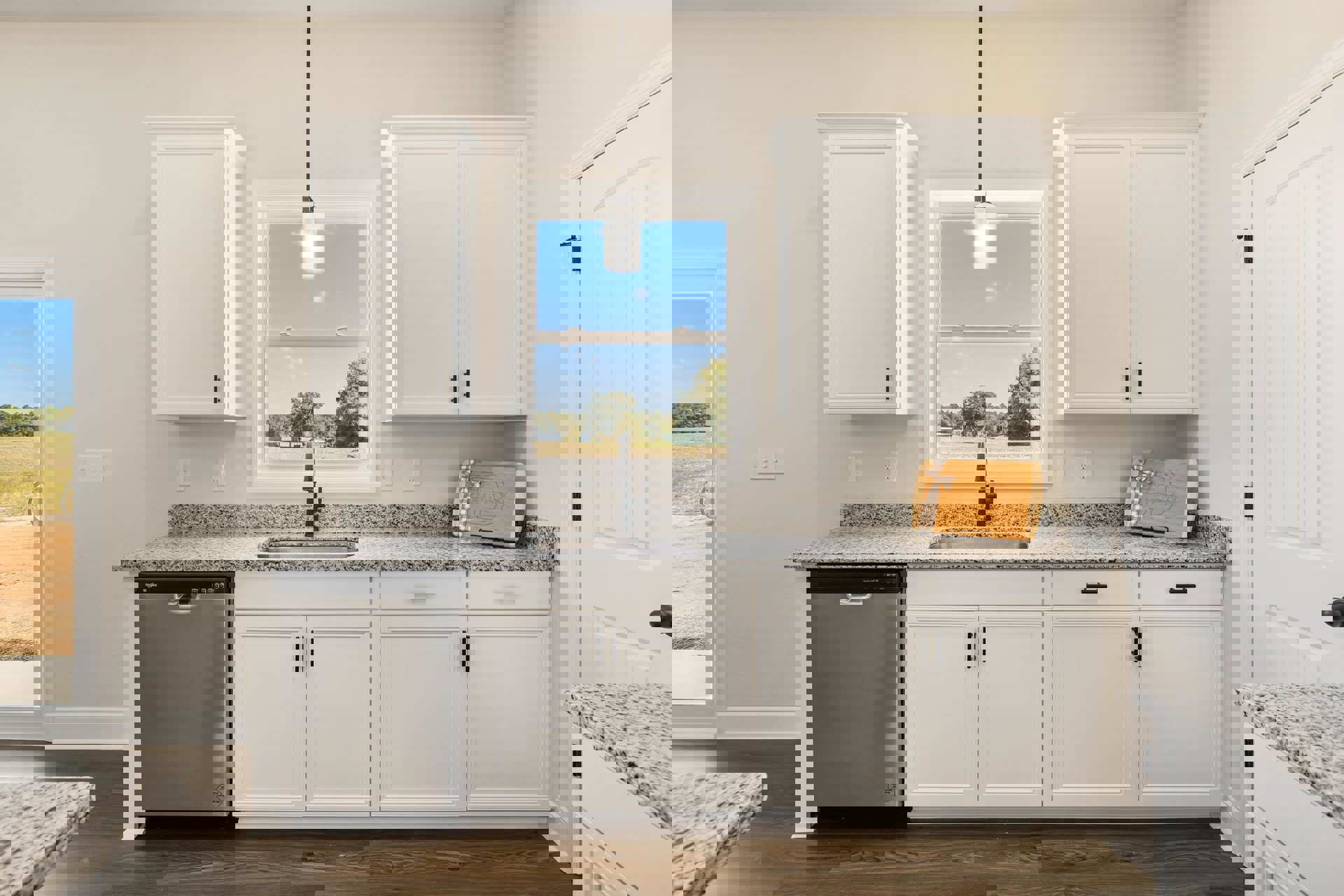 Modern kitchen featuring white cabinetry with black handles, stainless steel sink and dishwasher, wooden cutting board with a bow on the countertop, large window overlooking a