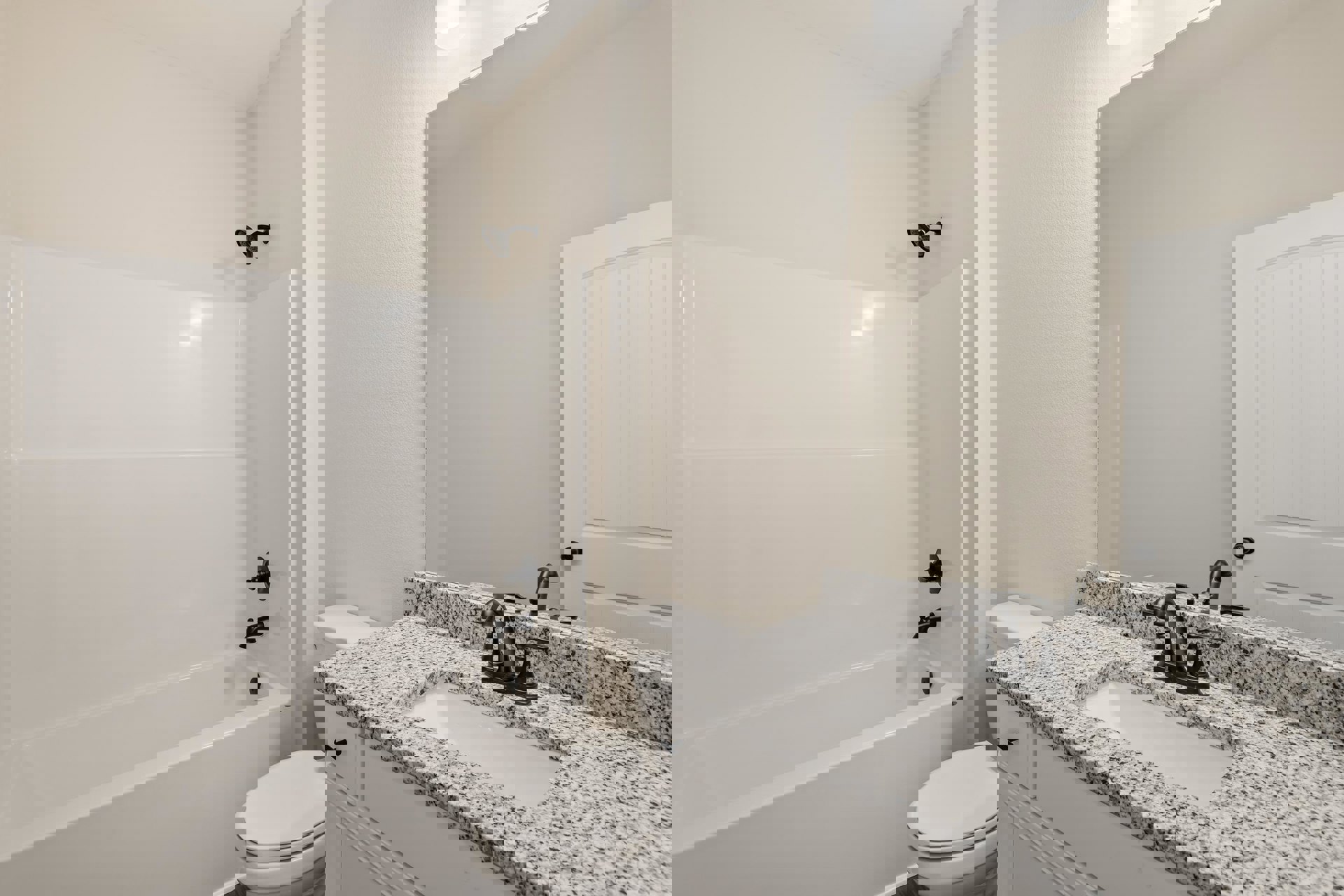 Bathroom with white paneled walls, modern sink and faucet, white toilet, and black shower head; tile flooring and minimal accessories visible.