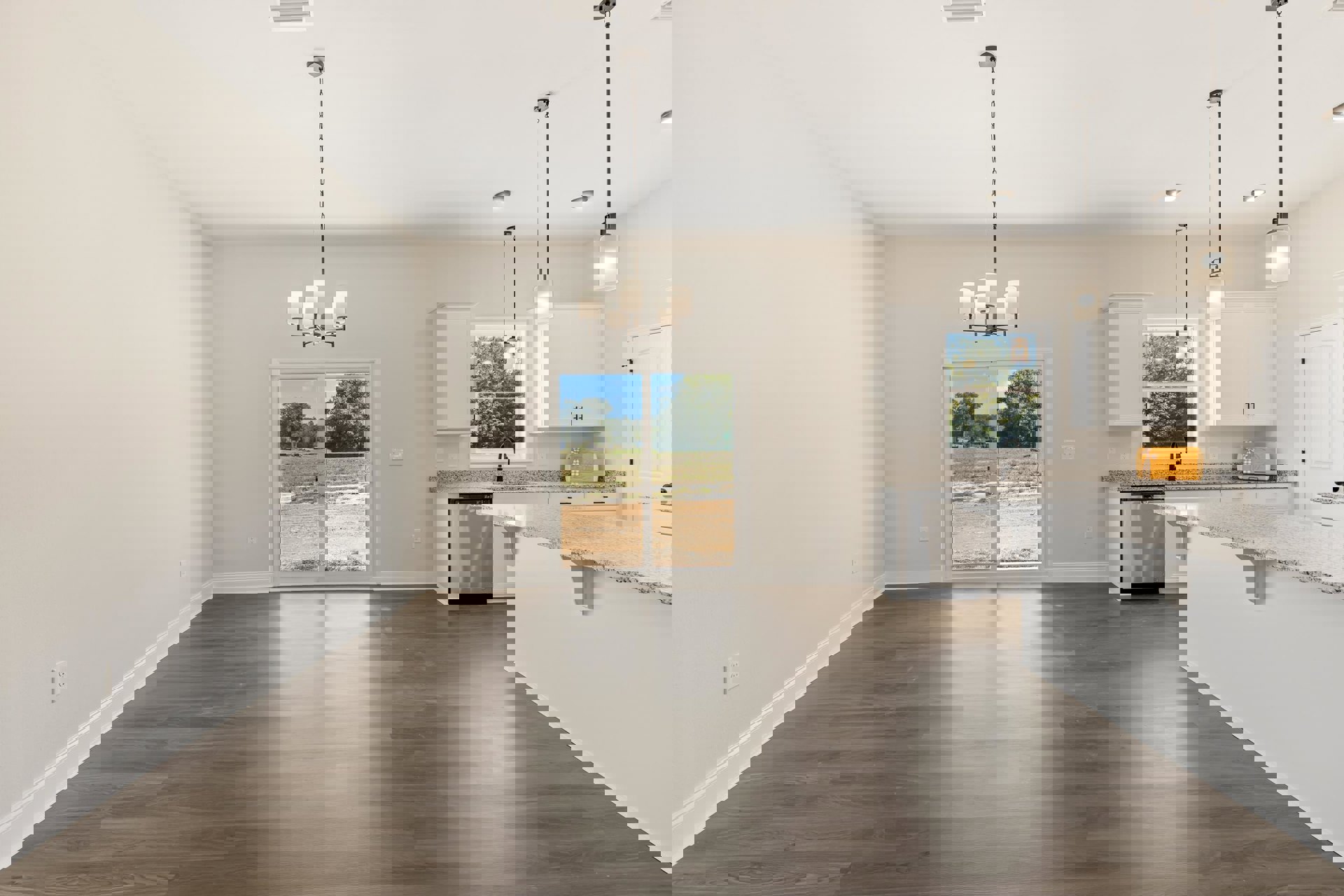 Open kitchen and dining area with light wood cabinetry, stone countertops, stainless steel appliances, and a large picture window overlooking a field and trees.