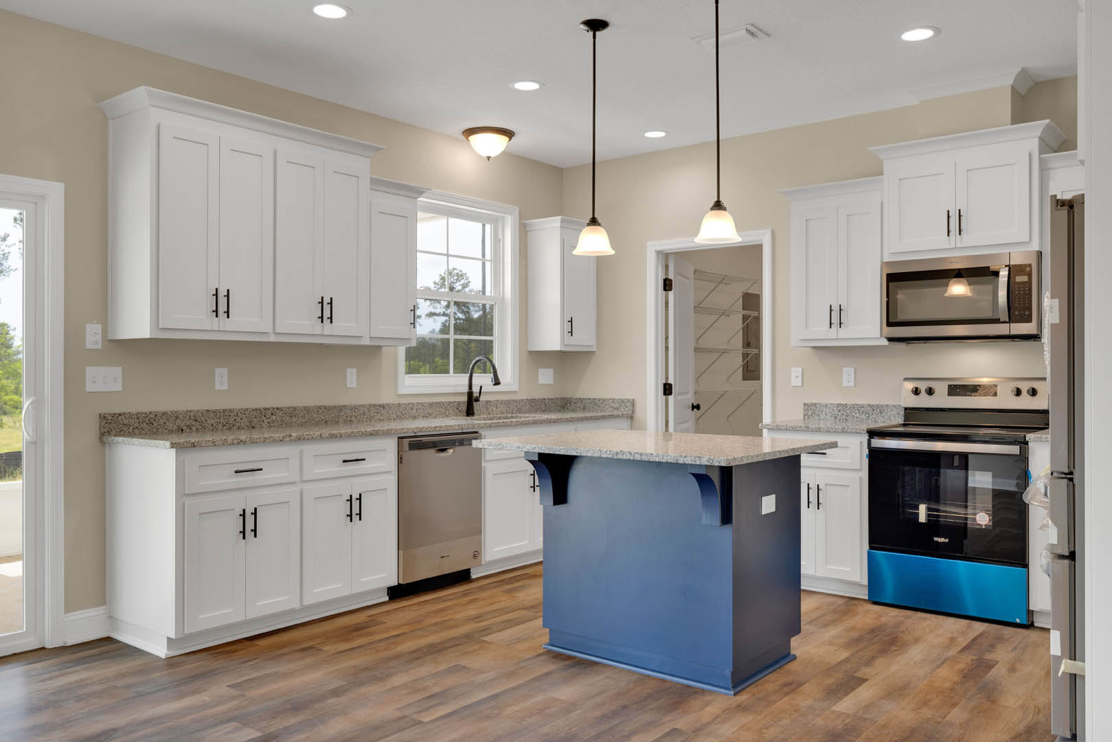 White kitchen cabinets, blue island with marble countertop, black and blue oven, ceiling light fixture, white wall with door, close-up of chrome faucet