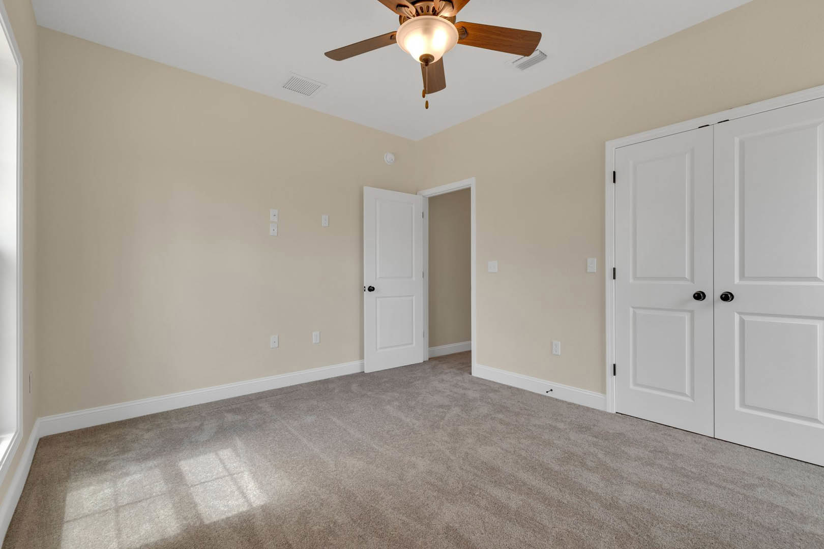 Carpeted room with white closet doors and black knobs, ceiling fan with light fixture, white entry door, white walls, and crown molding