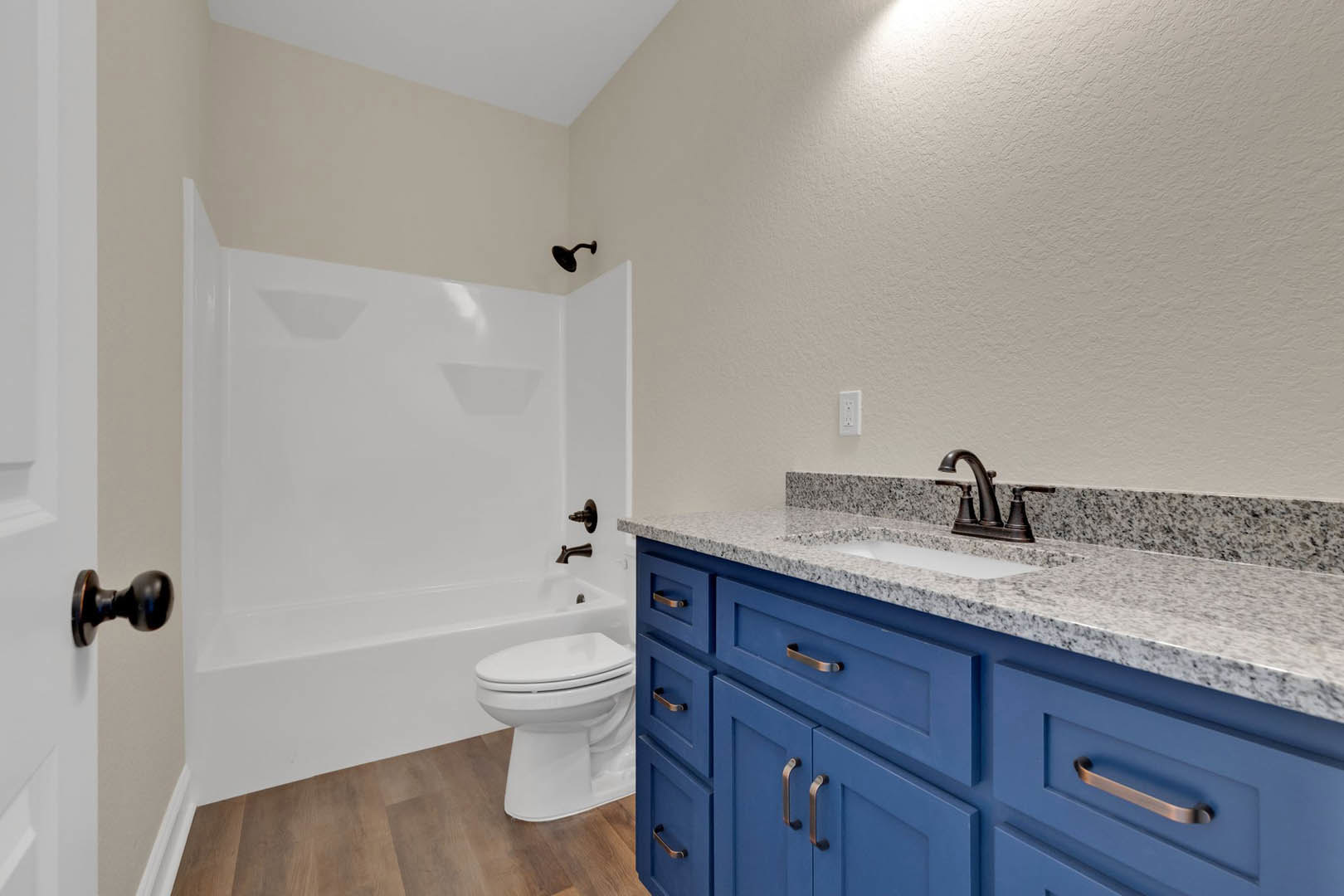 Blue bathroom cabinets with silver hardware, freestanding white bathtub, white toilet, light tile flooring, and white walls.
