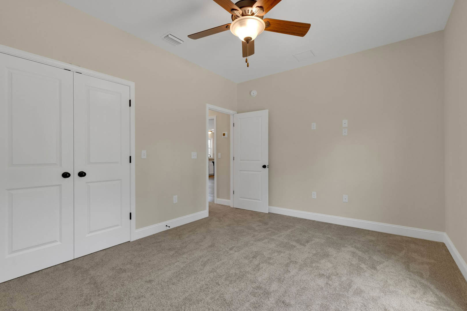 Carpeted room with white paneled doors featuring black knobs, ceiling fan with integrated light, white walls, and crown molding.