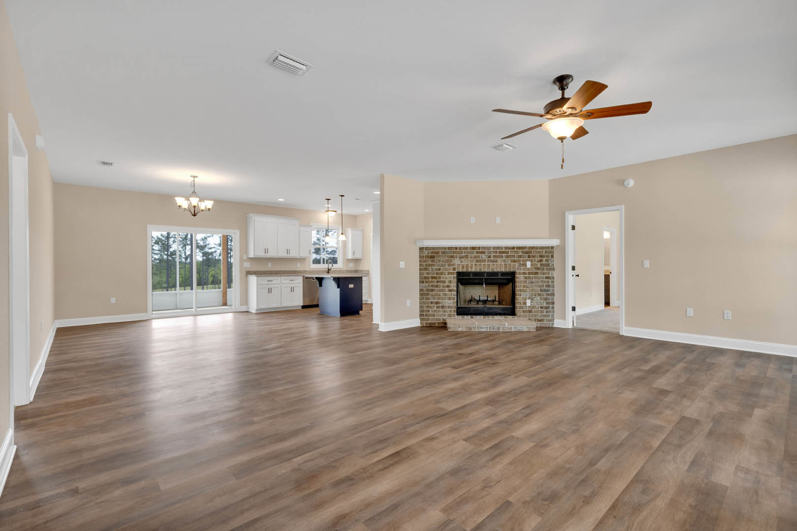 Spacious living room featuring hardwood floors, brick fireplace, ceiling fan with light fixture, large window overlooking trees