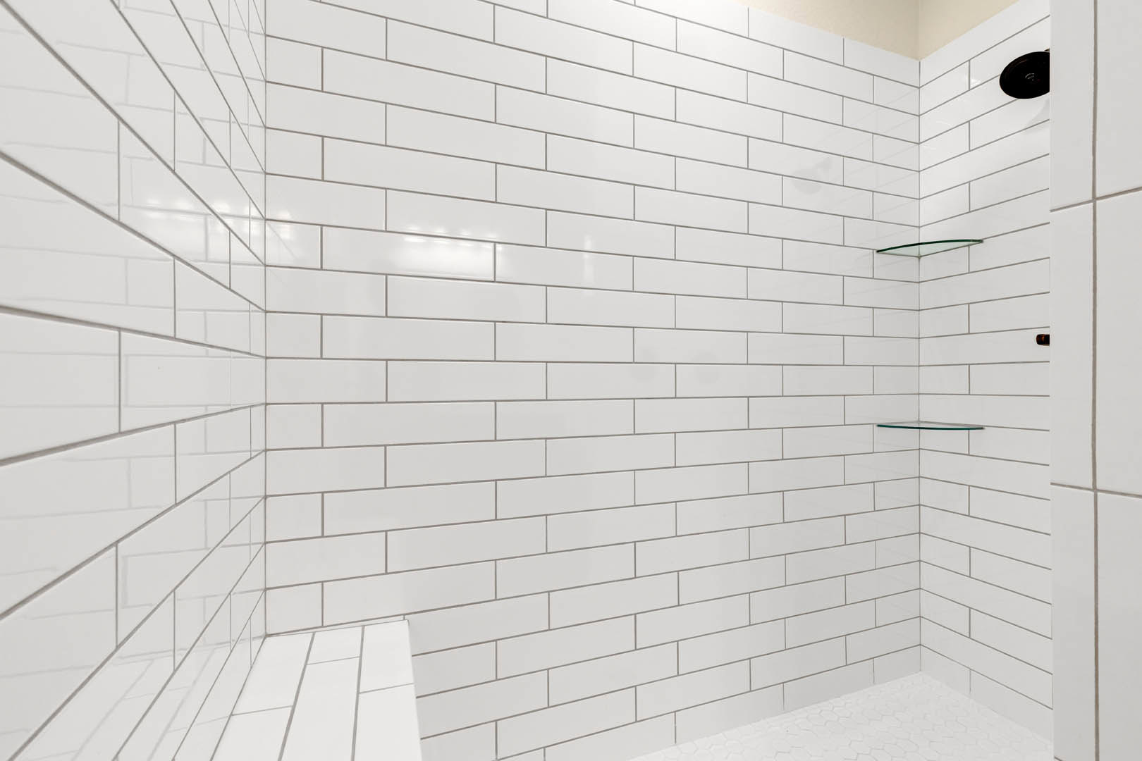 White tile shower with built-in glass shelves, white tile floor, and chrome shower pole