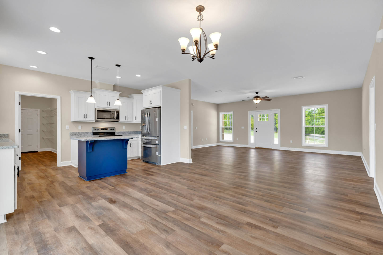 Spacious kitchen with hardwood flooring, blue island featuring marble countertop, stainless steel refrigerator, large window overlooking trees, white cabinetry, and recessed