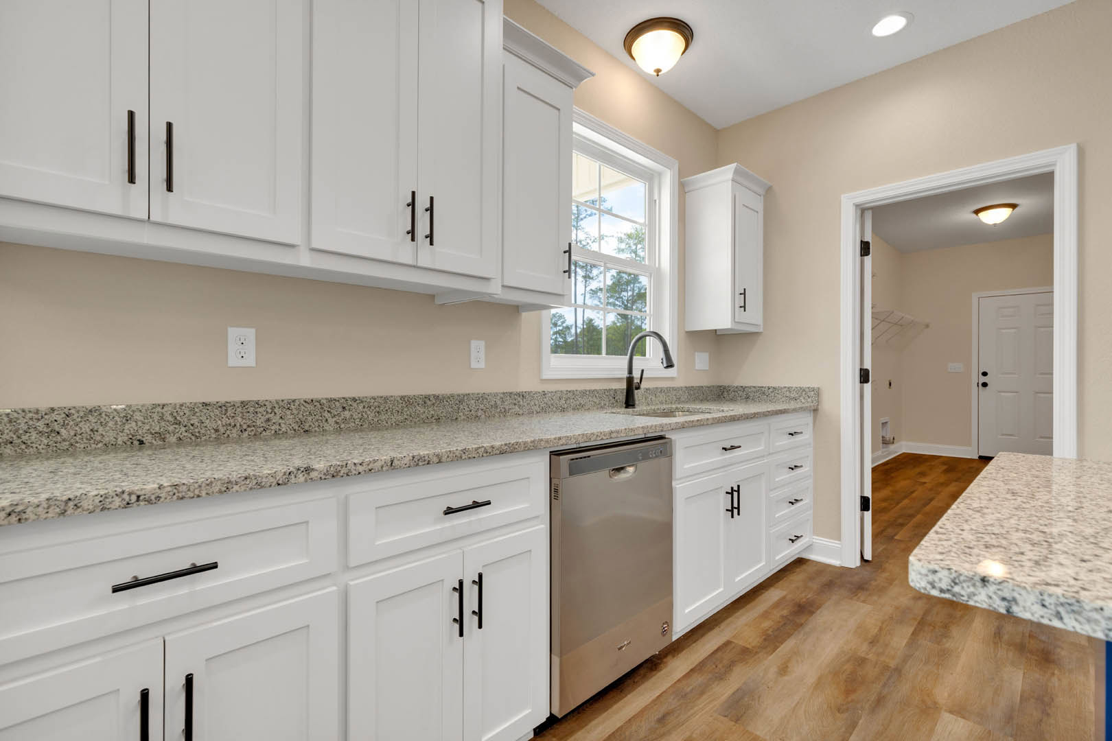 White kitchen with granite countertops, white cabinets, stainless sink, marble island, white refrigerator, window, and white door with black knobs.