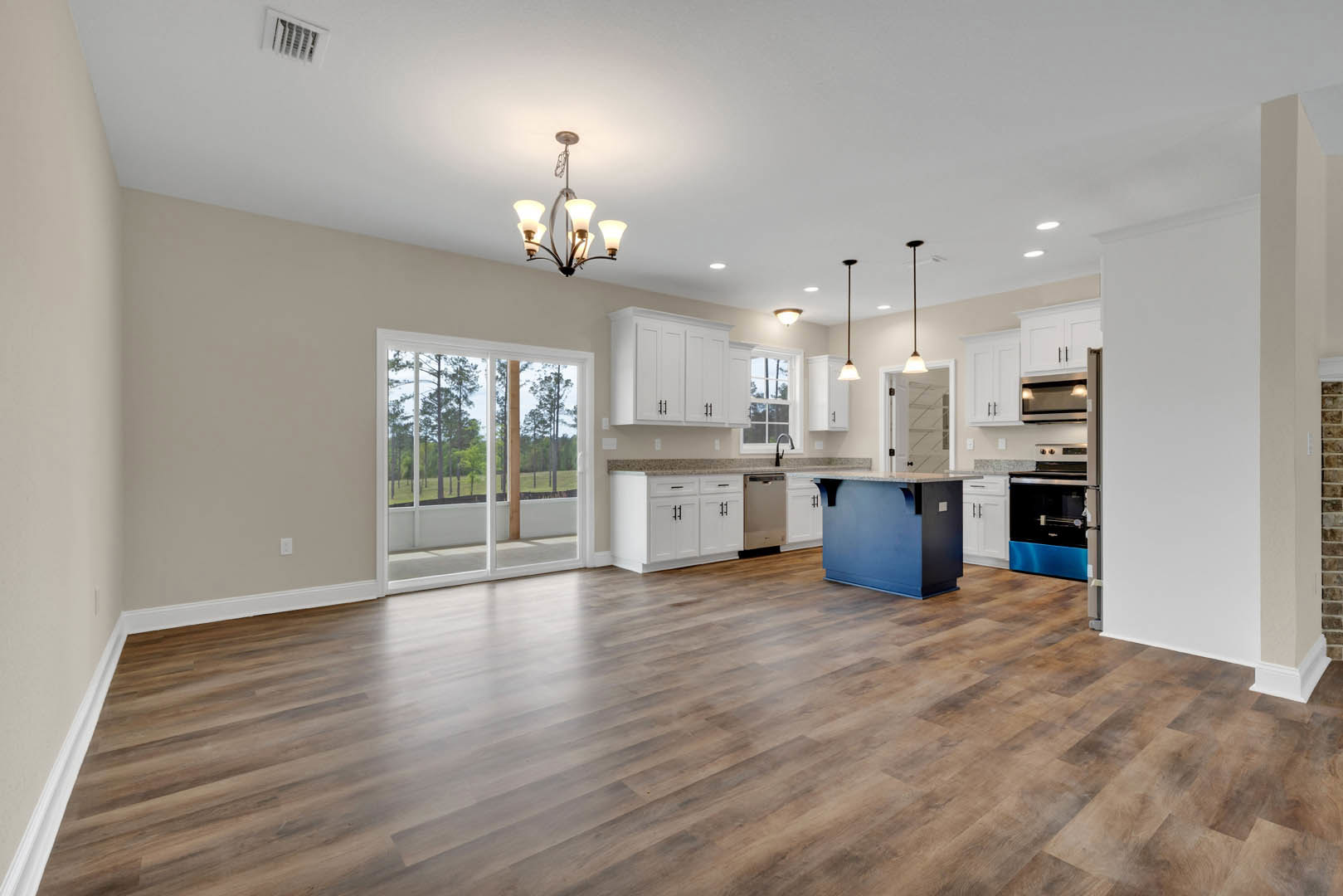 Open kitchen and dining area with hardwood floors, white cabinetry, blue refrigerator, marble-topped blue island, sliding glass door overlooking trees, modern chandelier, and white