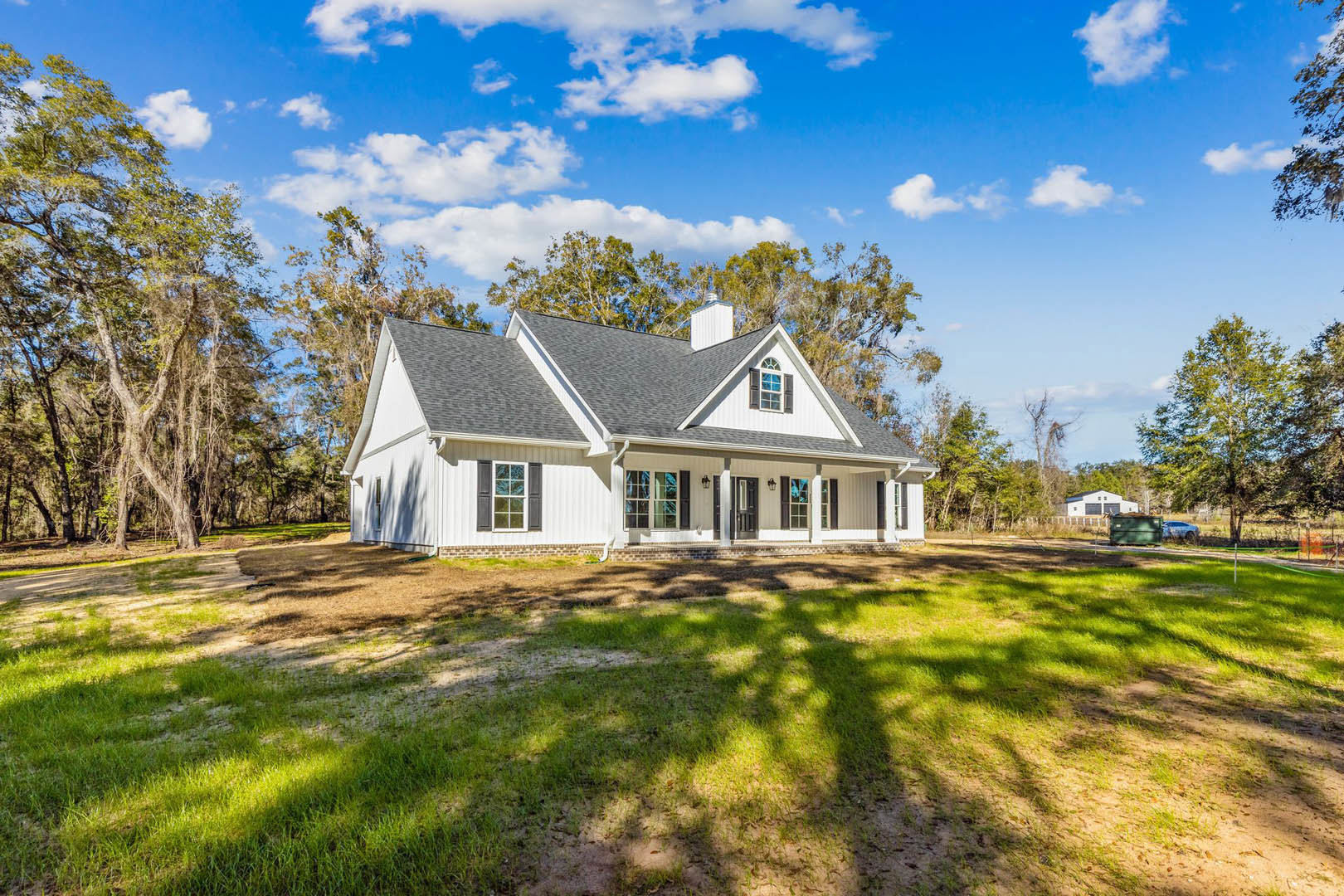 White-roofed house with white-framed windows and chimney, surrounded by green lawn and mature trees under partly cloudy sky