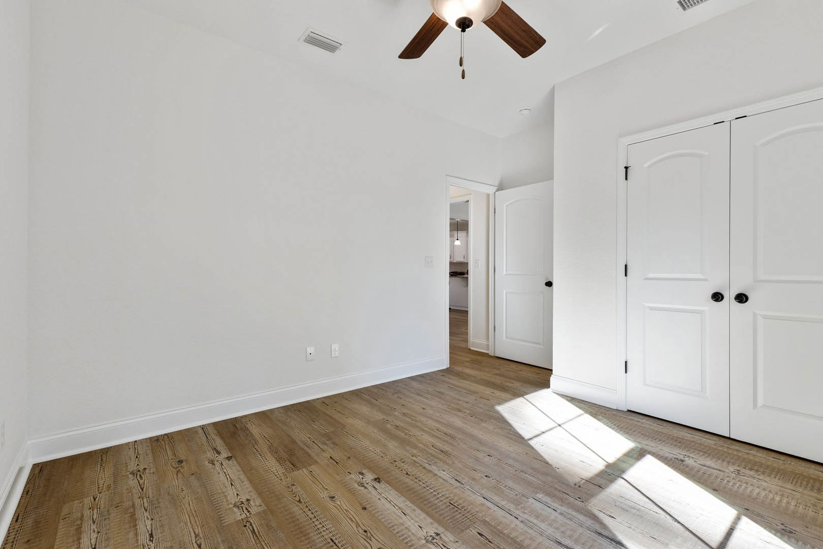 Ceiling fan with light fixture above hardwood floor, white door with black knob, white rug on wood flooring, plaster walls