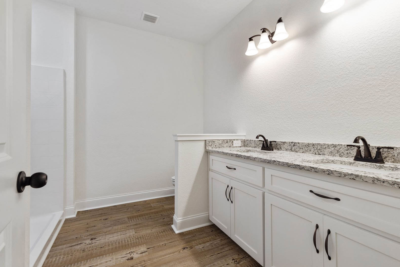 Bathroom featuring white cabinetry, marble countertops, wood flooring, three-light fixture, ceiling vent, white pillars, and close-up of a door knob.