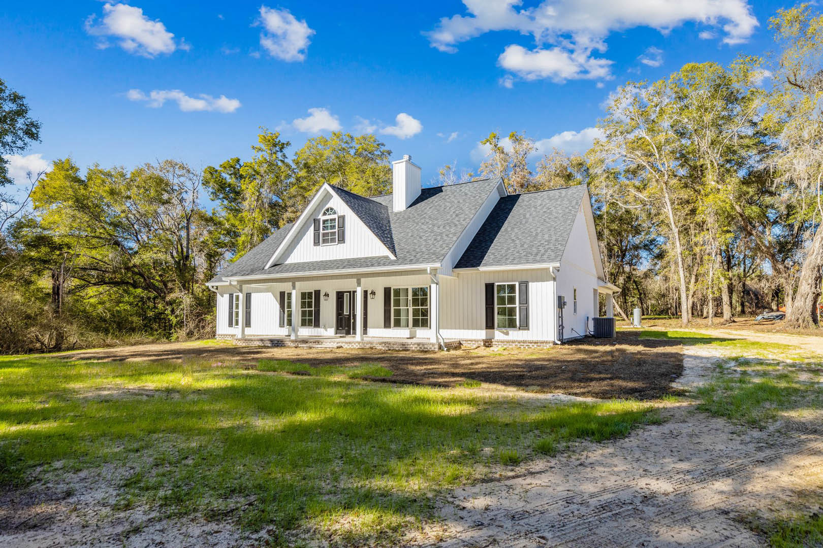 White siding home with prominent chimney, surrounded by leafy trees, manicured lawn in foreground, partly cloudy sky overhead