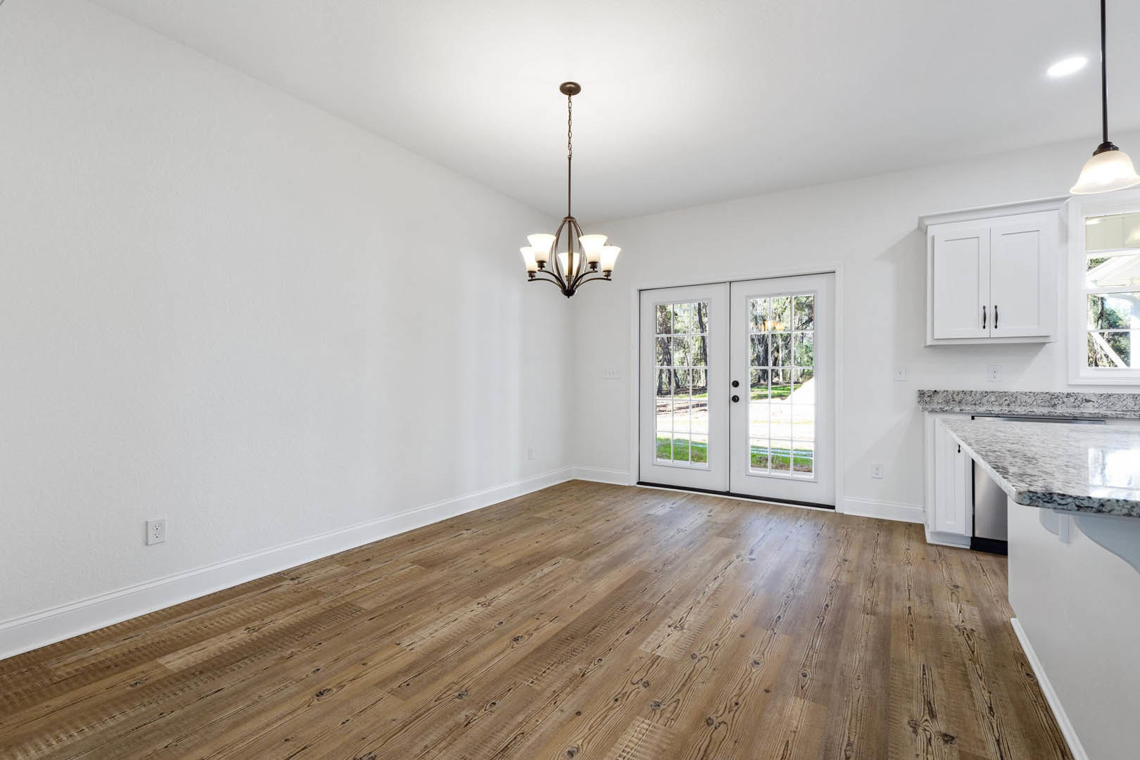 Wood flooring in a kitchen with a white cabinet, glass-paneled double doors, and a chandelier hanging from the ceiling.