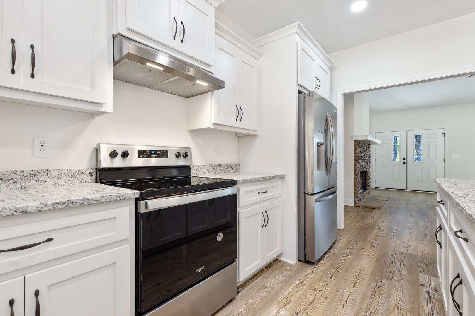 White kitchen with shaker cabinets, stainless steel stove and oven, quartz countertops, stainless steel refrigerator, glass-paneled double doors, and white wall outlet
