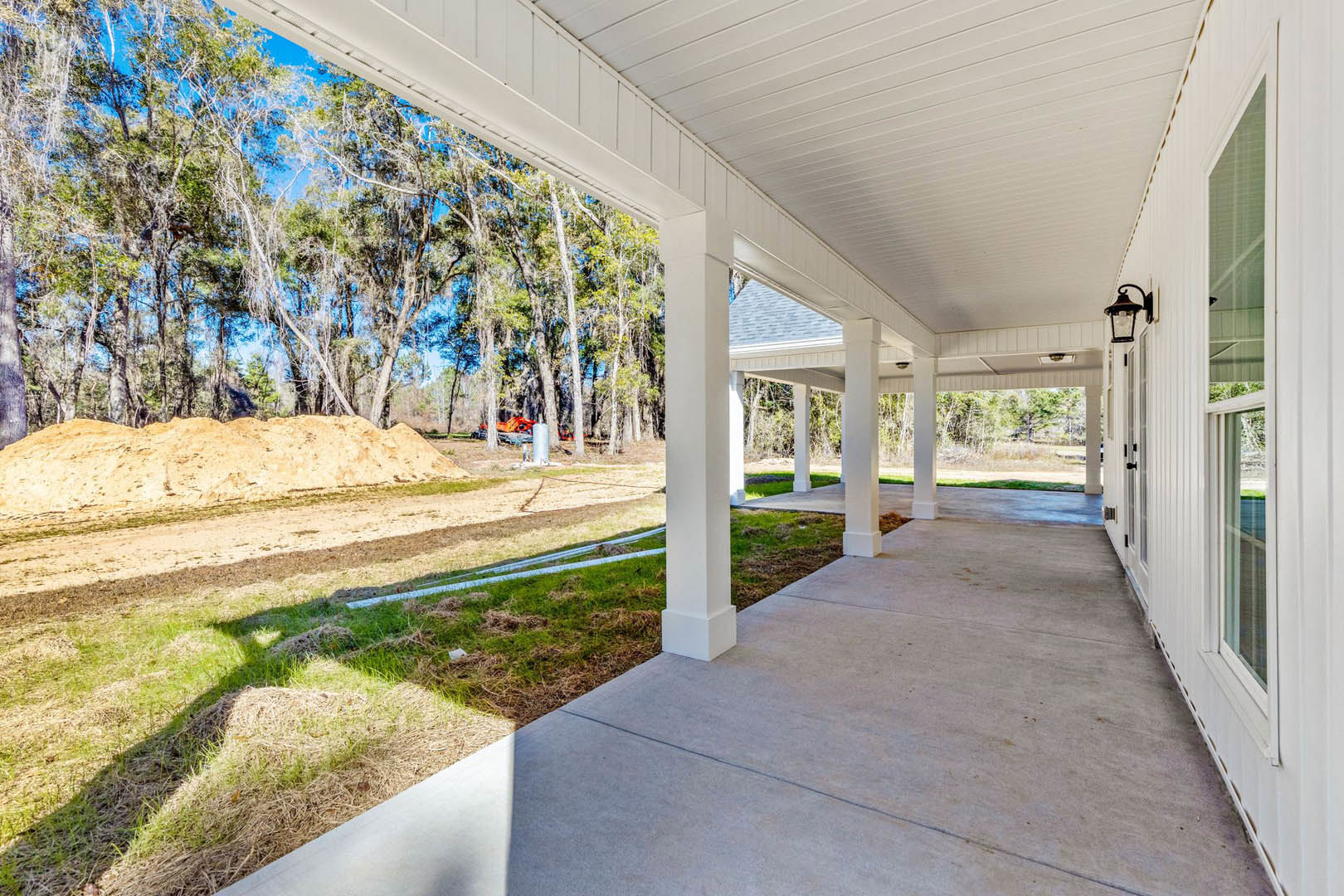 White porch with a single column, white roof, and lamp fixture overlooking a lawn with a dirt mound, bordered by trees and open sky.