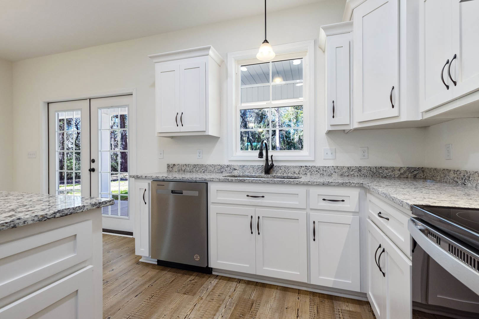 White kitchen cabinets and granite countertops, stainless steel refrigerator, stove top, window overlooking trees and porch, close-up of white cabinetry, countertop with window in